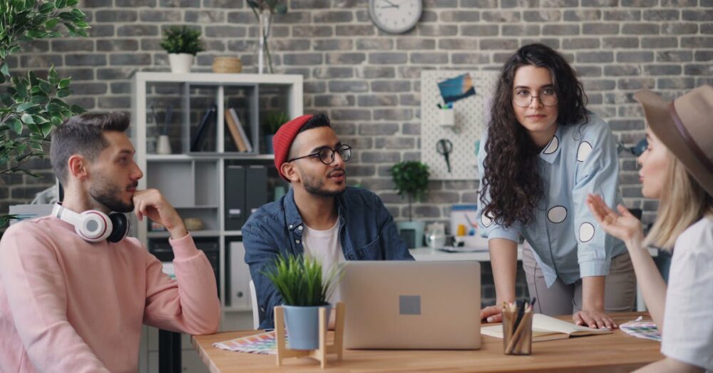 デザイナーやディレクターがGoogle Stitchを囲んでディスカッションしている様子。画面にはAIが生成した複数のデザイン案が表示され、ビジネスの意思決定が加速するシーン。