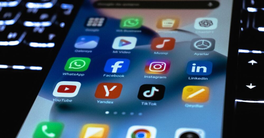 SNSの画面越しに、AIの進化について議論し、悲喜こもごもな反応を見せる世界中のユーザーたちの様子をイメージした、明るく活気のあるデジタルアート。