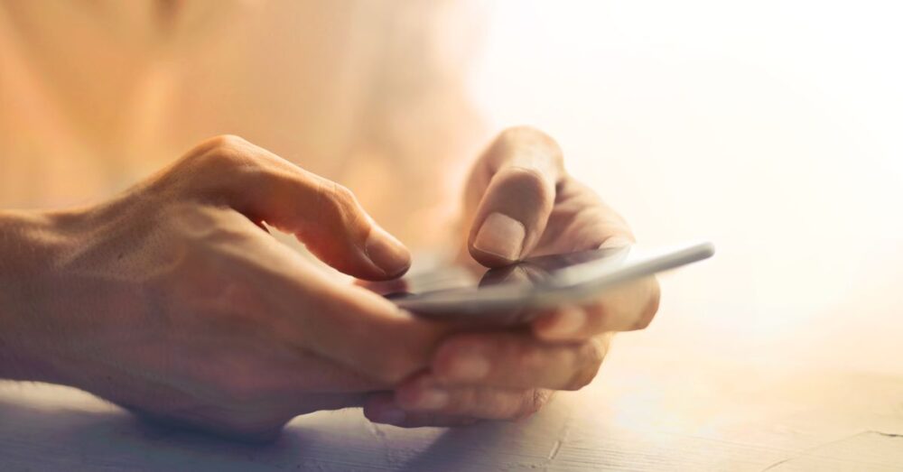 カフェで落ち着いてスマートフォンの画面を操作し、AIへの指示文（プロンプト）を入力している様子。自分好みにAIをカスタマイズするクリエイティブな時間を表現している。