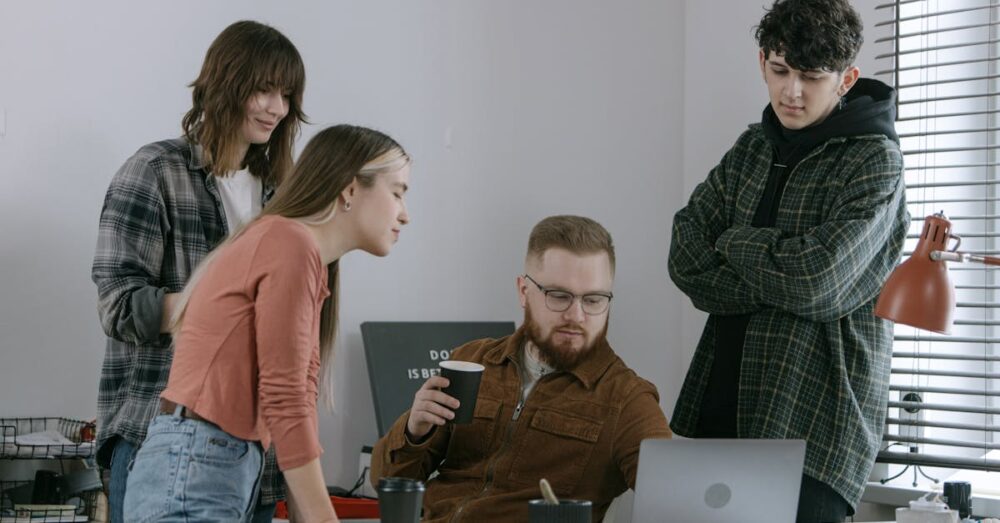 デザイナーやディレクターがGoogle Stitchを囲んでディスカッションしている様子。画面にはAIが生成した複数のデザイン案が表示され、ビジネスの意思決定が加速するシーン。
