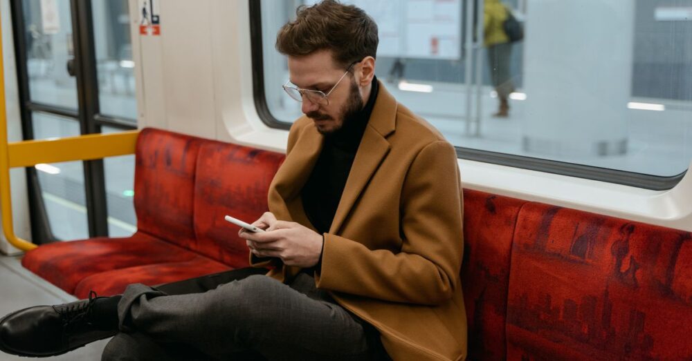 電車内でワイヤレスイヤホンを装着し、スマートフォンの画面を見ている人物の様子。NotebookLMの音声解説機能を使って、移動中に効率よく学習しているシーンを表現している。