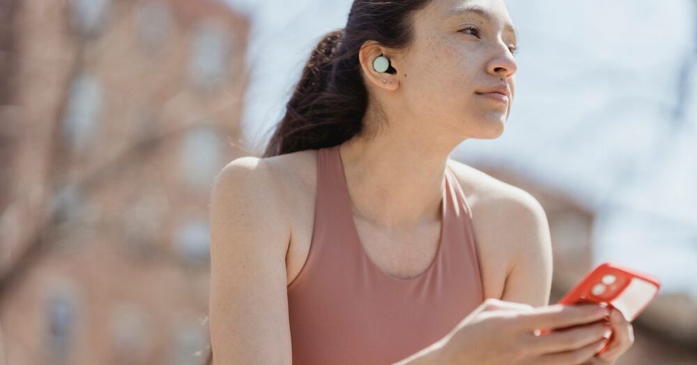 電車内でワイヤレスイヤホンを装着し、スマートフォンの画面を見ている人物の様子。NotebookLMの音声解説機能を使って、移動中に効率よく学習しているシーンを表現している。