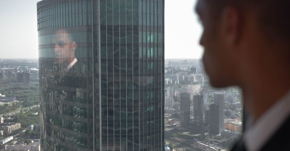 朝日が差し込むオフィスで希望を持って新しい働き方を迎えるベテラン会社員の背中。AIとの共存を象徴。